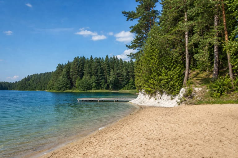 Sandy shore, wooden pier, and white lake-chalk bank at Gela Beach among pine trees