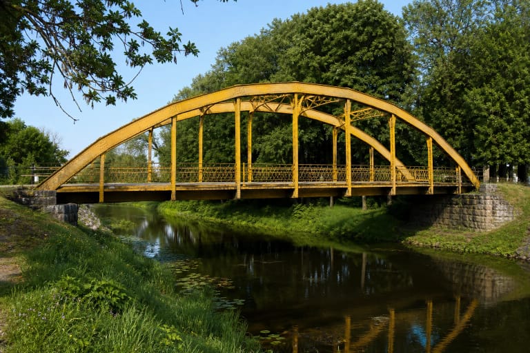 The yellow metal arch bridge across the Šyša before its removal for restoration in 2025