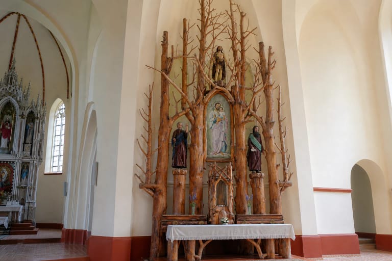 Side altar in Girdiškė Church rising in stripped oak trunks and interlaced natural branches beneath the pale vaults