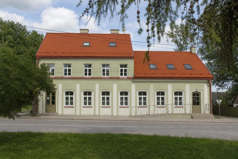 Gražutės regioninio parko lankytojų centro ilgas šviesiai žalias fasadas su raudonų čerpių stogu ir pandusu Salake