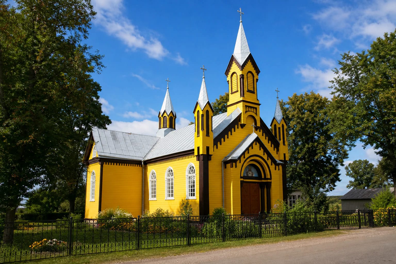 Yellow wooden Gudžiūnai Church of the Sacred Heart of Jesus with white spires and a flower garden