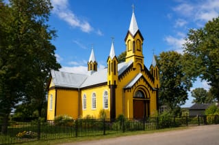 Жёлтый деревянный костёл Пресвятого Сердца Иисуса в Гуджюнае с белыми шпилями и цветником