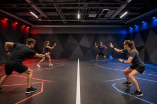 Two HADO players wearing lightweight glasses and hand sensors on a lit indoor sports court