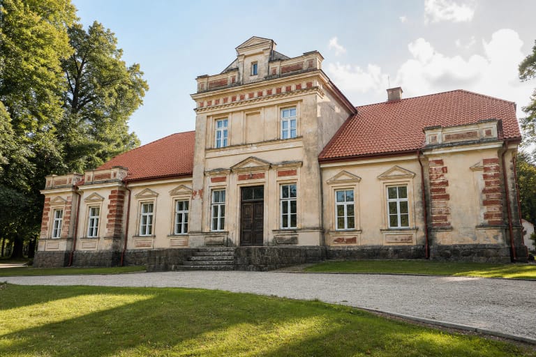 Jakiškių dvaro rūmai su šviesiu fasadu, raudonu stogu ir brandžiais medžiais