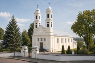 Light-coloured twin-towered facade and churchyard gate of the Church of St James the Apostle in Jonava on a summer day