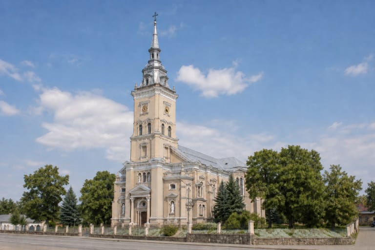 Church of the Assumption of the Blessed Virgin Mary in Joniškis with one tall tower, clocks on its two visible faces, and a pale Historicist façade