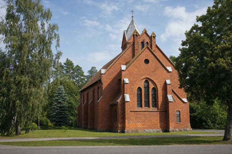 Juodkrantės evangelikų liuteronų bažnyčios raudonų plytų fasadas ir žemas bokštas su metaline smaile