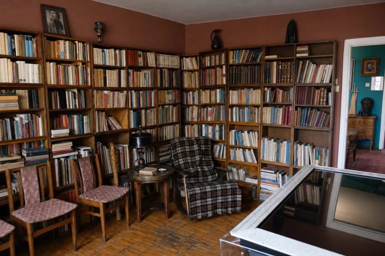 Juozo Miltinio memorialinio buto biblioteka su knygų pilnomis medinėmis lentynomis, languotu krėslu ir senais baldais