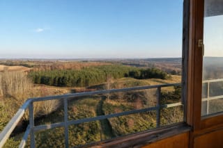 Kačergų kalno panorama pro apžvalgos bokšto langą į banguotas pasienio kalvas ir miškus