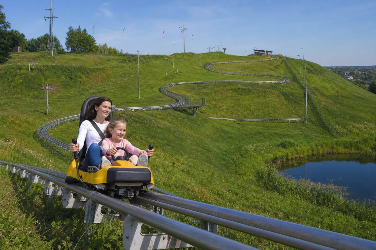 Yellow alpine-coaster sled descending silver rails on the green slope of Kalita Hill in Anykščiai
