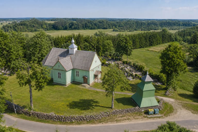 Šviesiai žalia medinė Kalnalio Šv. Lauryno bažnyčia, atskira trijų tarpsnių varpinė ir akmenų tvora Salanto slėnio pakraštyje