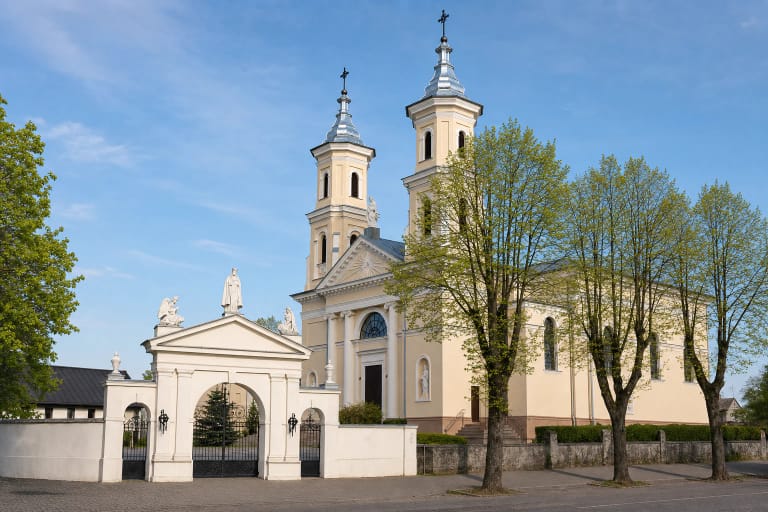 Kalvarijos Marijos Vardo bažnyčios šviesus klasicistinis dvibokštis fasadas ir skulptūromis puošti balti šventoriaus vartai