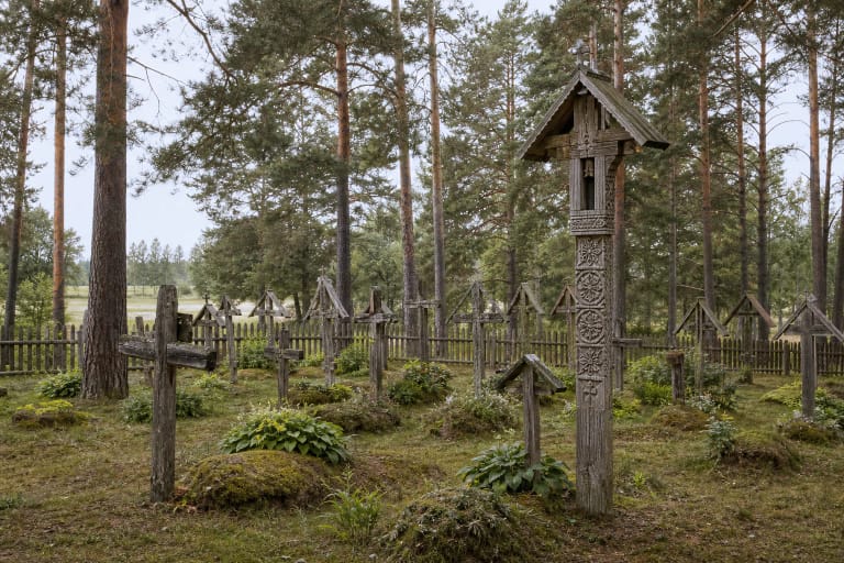 Lithuanian cemetery with wooden crosses, krikštai, a chapel-post, stone grave markers, gates, and old trees