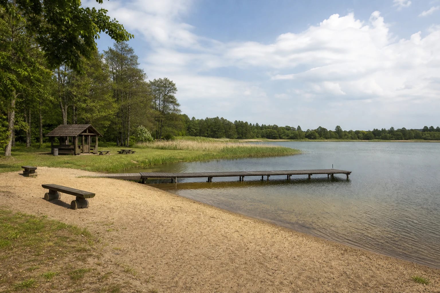 Sandy recreation area on Lake Kapstatas with a timber pontoon bridge, shelter, and low wooded shore