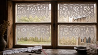 White cut paper curtains with bird, plant, sunburst, and toothed ornaments on a wooden rural window