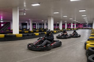 Kartlando Kaune vidaus trasa su trimis kartingais, geltonai juodais padangų barjerais ir baltais pastato stulpais