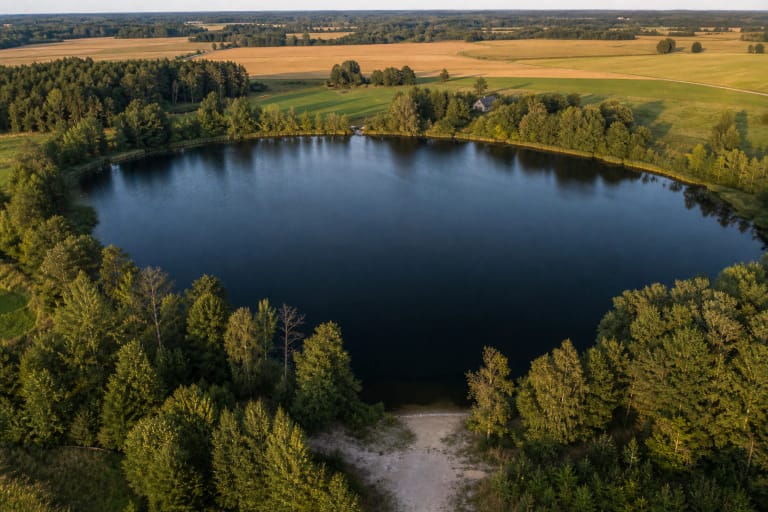Deep blue-green Kašučiai Lake with a stony northern shore, small bathing place, woodland, and meadows