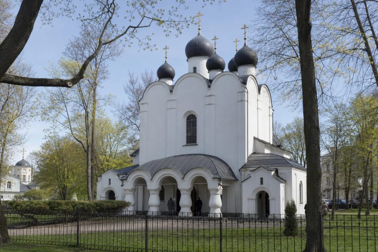 Белый Каунасский собор Благовещения с пятью тёмными луковичными куполами и арочной колоннадой среди деревьев парка Рамибес