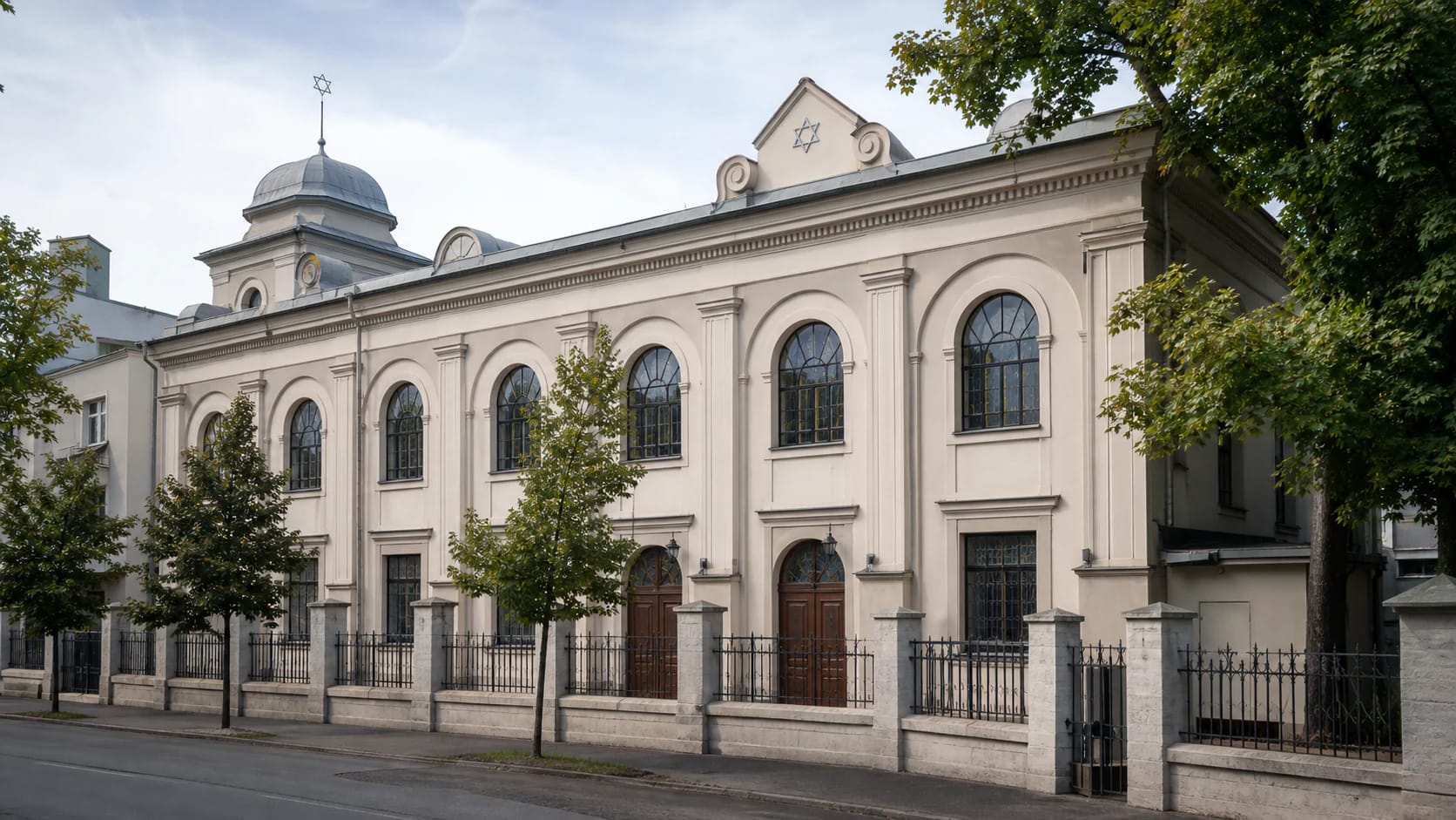 Light historicist facade of Kaunas Choral Synagogue with arched windows, Star of David, dome, and metal fence on E. Ožeškienės Street