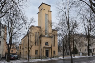 Yellowish modernist facade of Kaunas Evangelical Reformed Church with central tower, arched entrance window, and narrow vertical windows