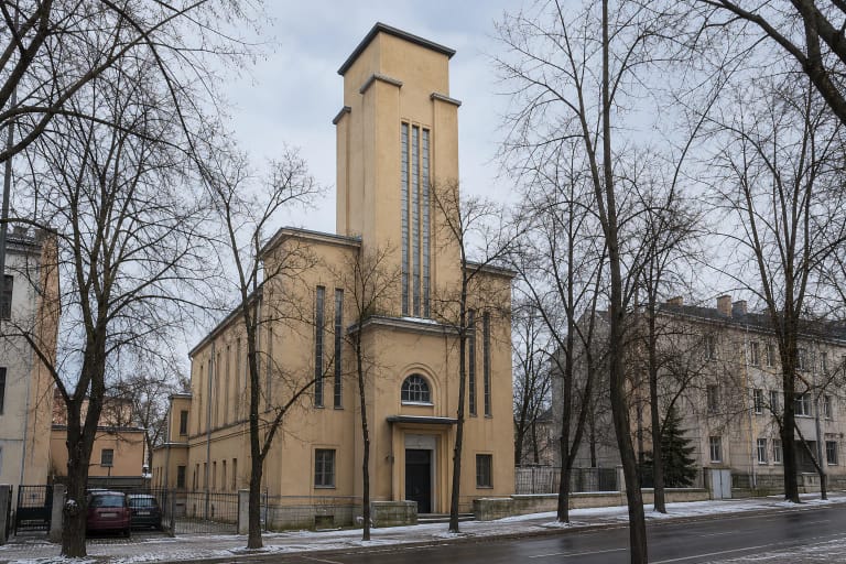 Kauno evangelikų reformatų bažnyčios gelsvas modernistinis fasadas su centriniu bokštu, arkinio lango portalu ir siaurais vertikaliais langais
