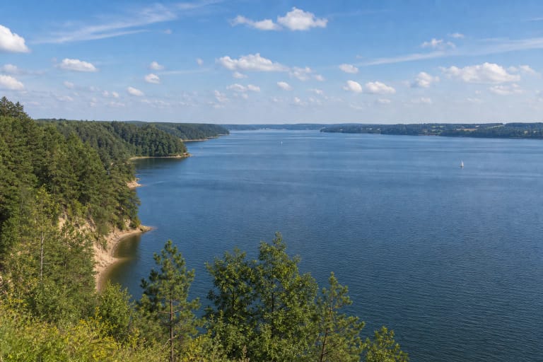 Wide water of Kauno Marios with wooded slopes and an outcrop shore in the regional park