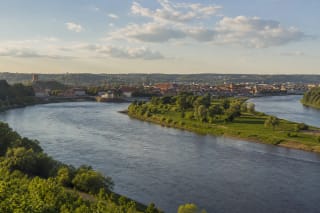 The Nemunas and Neris confluence with green riverbanks, Kaunas Old Town, and a distant castle silhouette