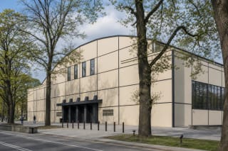 Restored light facade of Kaunas Sports Hall with dark steel-line grid among the trees of Azuolynas