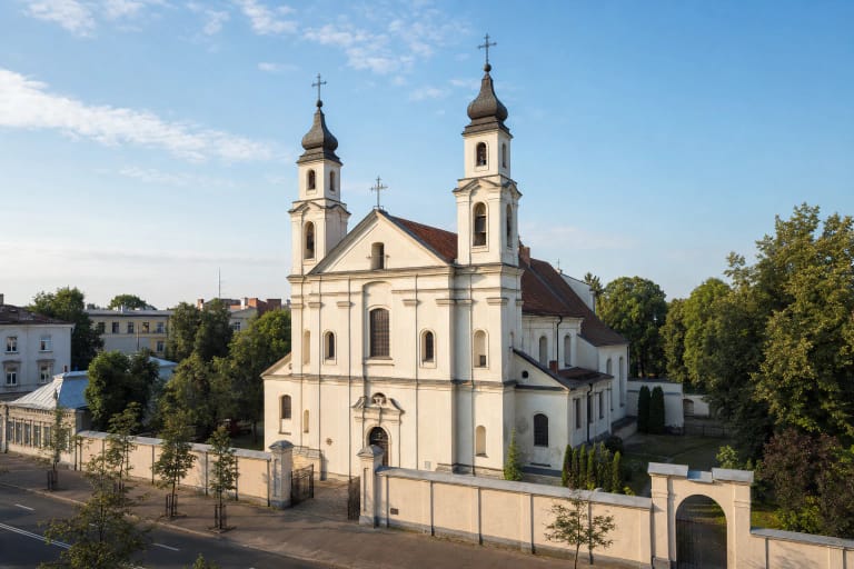 Šviesi dvibokštė Kauno Šv. Kryžiaus Karmelitų bažnyčia už žemos šventoriaus sienos Gedimino gatvėje