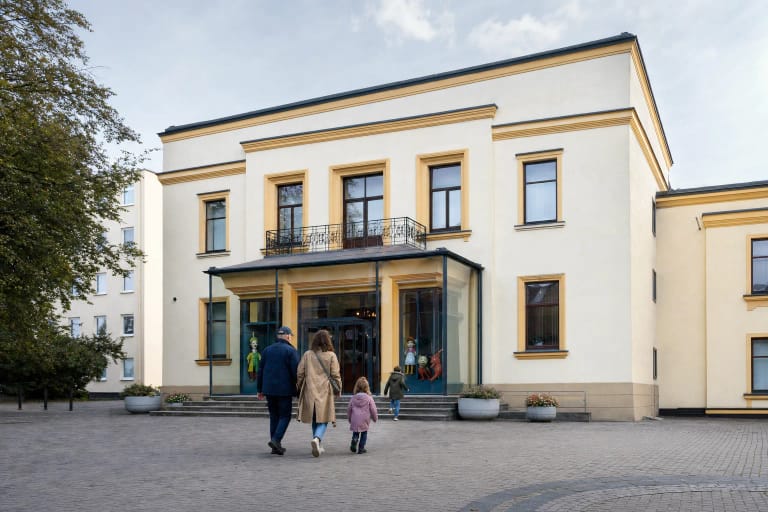 Šviesus Kauno valstybinio lėlių teatro pastatas buvusio Odeon kino teatro kieme su šeima prie įėjimo