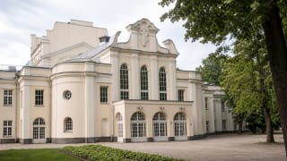 Kauno valstybinio muzikinio teatro kremiškas neobarokinis fasadas Miesto sode su trimis arkiniais langais, banguotu frontonu ir medžiais