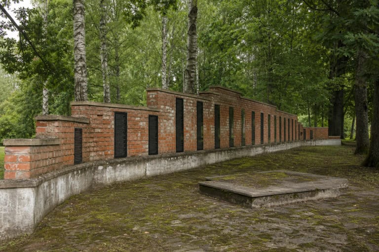 Kaušėnų memorialo iš senų raudonų plytų sumūryta Atminties siena su juodomis vardų plokštėmis medžių paunksmėje