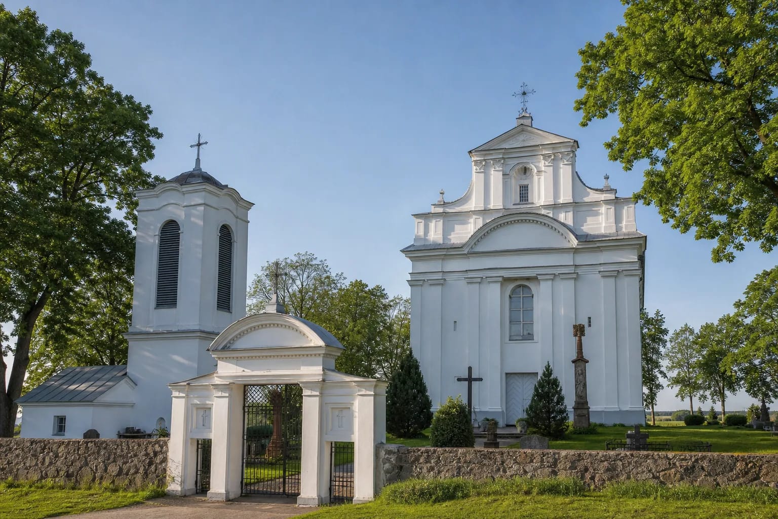 Белый однонефный костёл в Казокишкяй без башни, отдельная каменная колокольня и арочные ворота погоста среди взрослых деревьев