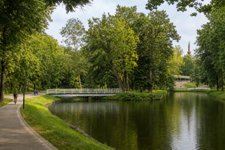Dotnuvėlė pond in Kėdainiai Central Park with white footbridges, mature trees, an amphitheatre, and the distant minaret