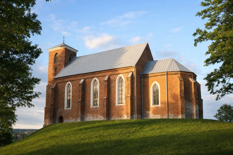 Raudonų plytų Kėdainių Šv. Jurgio gotikinė bažnyčia ant žalios kalvos su baltais langų apvadais ir šviesiu stogu