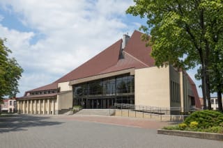 Angular pale Kelmė Cultural Centre building with a broad glass entrance, red-brown roof, and ramp