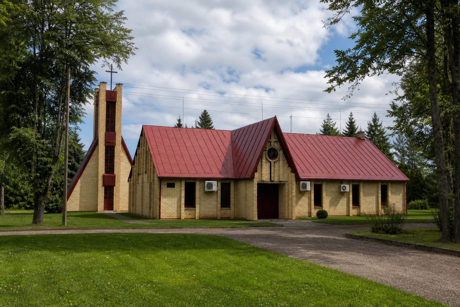 Low yellow-brick Keturvalakiai church with red multi-gabled roofs and a separate open-slat bell tower