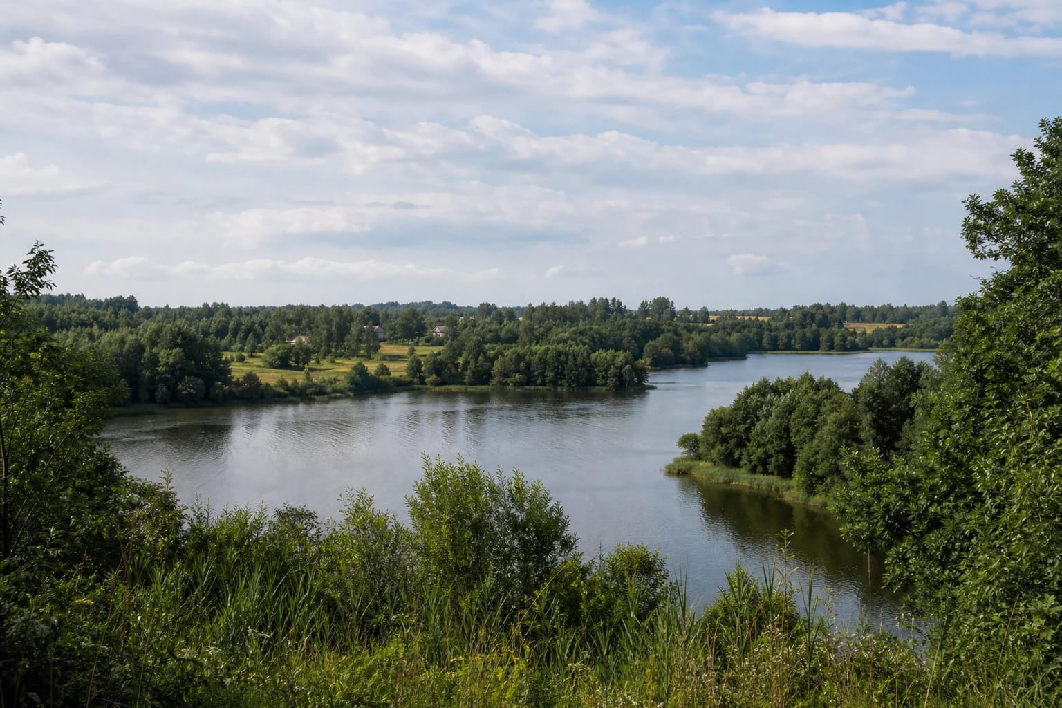 Kiemeliai Lake between tree-lined shores, fields, and the Kiemeliai village area