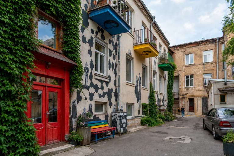 Kiemo galerijos Kaune gyvenamas kiemas su gebenėmis, raudonomis durimis, spalvotais balkonais ir portretais ant sienų