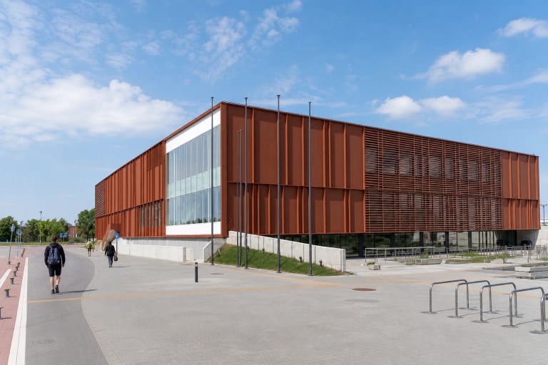Rūdžių raudonumo metalo plokštėmis dengtas modernus Klaipėdos baseino pastatas su stikline centrine fasado dalimi