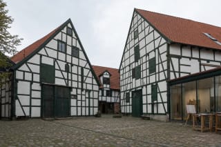 Cobbled KCCC Art Yard enclosed by white half-timbered warehouses with dark beams and red tile roofs