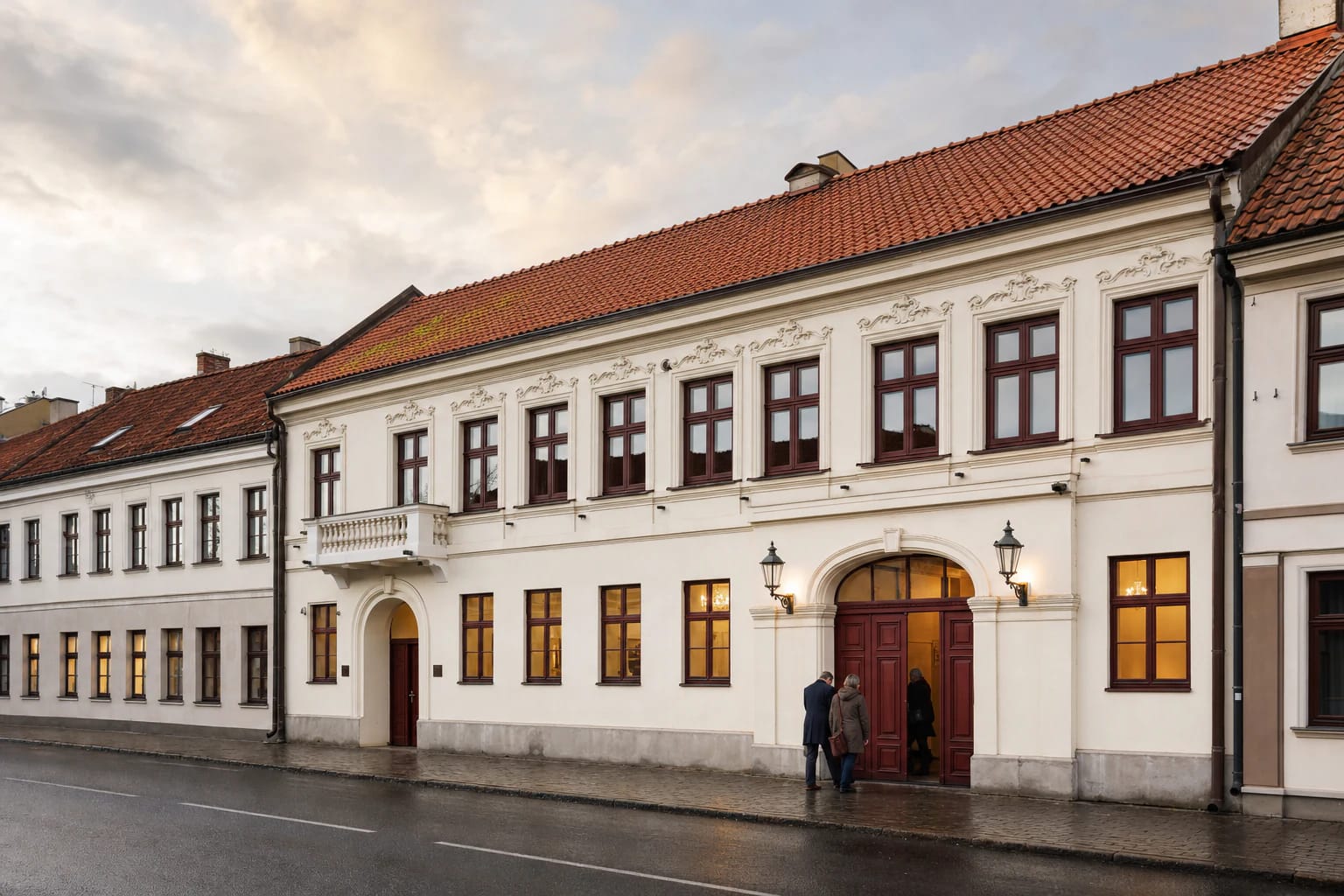 Klaipėdos koncertų salės istorinis šviesus fasadas su tamsiai raudonais langais ir čerpiniu stogu po lietaus