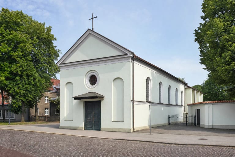 White-rendered facade of Christ the King Church in Klaipėda with a round window, bronze doors and a cross on Bokštų Street