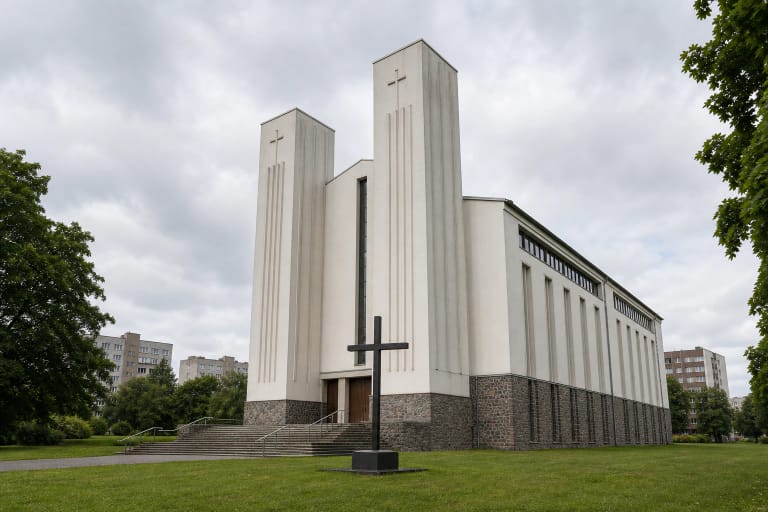 Klaipėdos Šv. Juozapo Darbininko bažnyčios balti siaurėjantys bokštai, platūs laiptai ir juodas kryžius pievoje