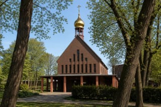 Церковь Всех русских святых в Клайпеде из клинкерного кирпича с крутой крышей, узкими окнами и небольшим золотым куполом среди деревьев парка