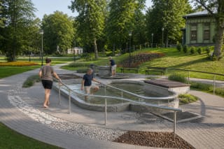 Oval mineral-water pool, barefoot sensory path, and benches in the green surroundings of Kneipp Garden in Birštonas