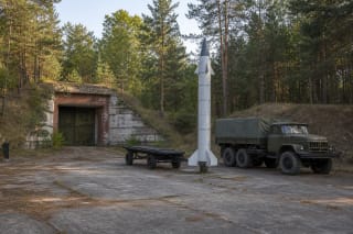 Макет ракеты, военный грузовик и покрытые землёй ангары на лесной площадке ракетной базы Копустеляй