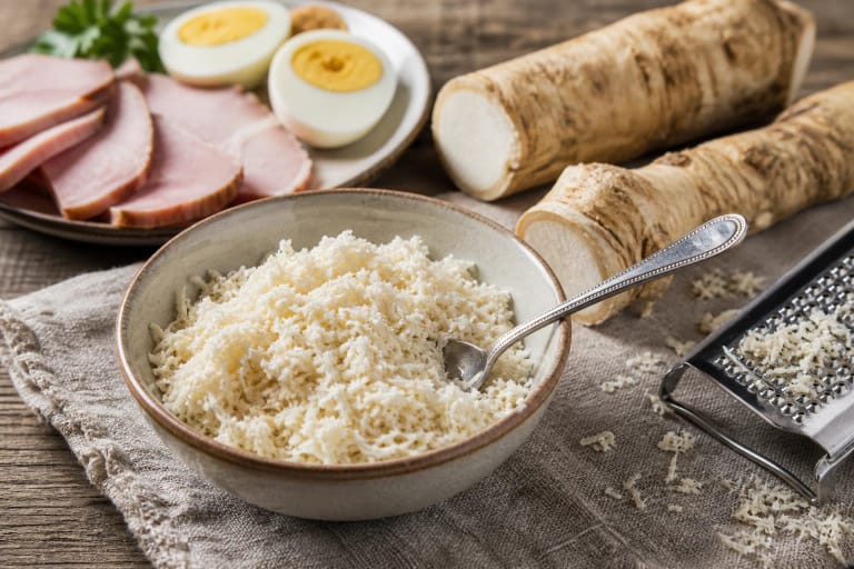 Freshly grated horseradish in a clay bowl with horseradish root, boiled eggs, and rye bread