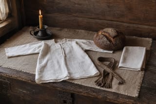 A historical Lithuanian baptism table with white baptismal clothing, bread, and a candle