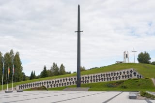 Kryžkalnio partizanų memorialo kalavijo formos obeliskas, vardų siena ir akmenimis grįsta ceremonijų aikštė žaliame šlaite